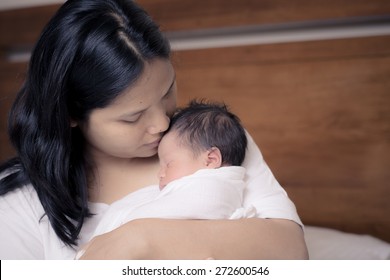 Asian Mother Holds Close And Kisses Her Mixed Race 10 Day Old Newborn Baby Boy In Her Bedroom