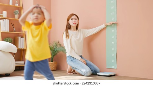 asian mother is leading her child son to measure height and she is worried about his development - Powered by Shutterstock