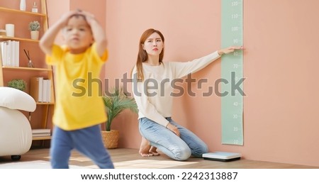 asian mother is leading her child son to measure height and she is worried about his development