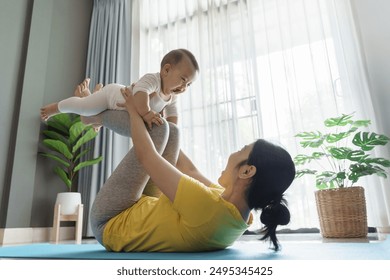 Asian Mother lifting smiling baby during exercise at home. Indoor lifestyle photography with plants in background. Family and fitness concept - Powered by Shutterstock