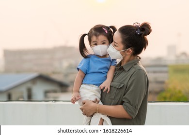 Asian mother and little young daughter wearing mask for prevent dusk pm 2.5 bad air pollution on deck in Bangkok city Thailand 2020. 