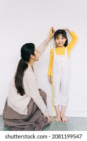 Asian mother is measuring her daughter's height