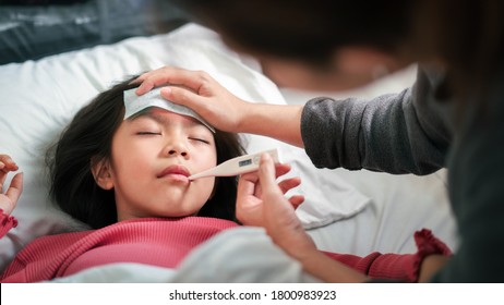 Asian mother measuring temperature girl with digital thermometer in her mouth on bed at morning time, Sick child have cool towel for reduce high fever,  Selective focus, Healthy and infection concept - Shutterstock ID 1800983923