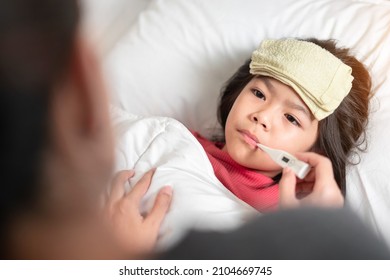 Asian Mother Measuring Temperature Girl With Digital Thermometer In Her Mouth On Bed At Morning Time, Sick Child Have Cool Towel For Reduce High Fever,  Selective Focus, Healthy And Infection Concept