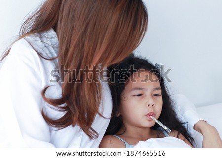 Asian mother measuring temperature of her daughter. child is sick with a high fever and is hot in bed. Mother holding a thermometer Take care of your child with love and care. 