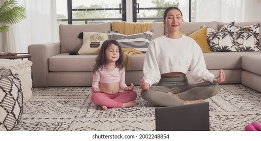 Asian Mother And Mixed Race Daughter Exercising Yoga Online Virtual Streaming Lesson At Home During Covid Pandemic, Family Remote Learning Together, Health Care, Healthy Lifestyle Concept