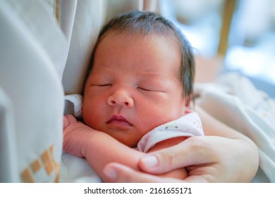 Asian mother with newborn baby in the hospital. Two day old of little asian newborn baby sleeping and smiling in mother's embrace.