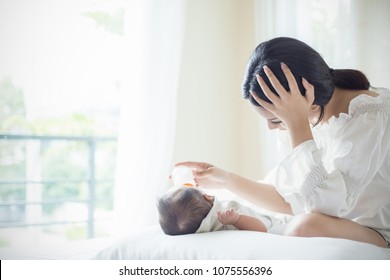 Asian Mother Nursery Feeding Bottle Of Formula Milk To Newborn Baby In Bed Suffering From Post Natal Depression. Health Care Single Mom Motherhood Stressful Concept.