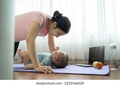 Asian Mother playing with baby on yoga mat in living room, engaging in playful exercise, joyful bonding moment - Powered by Shutterstock