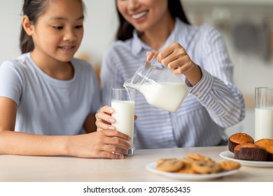 Asian mother pouring fresh milk for her cute teen daughter, pretty girl having breakfast with her young mom, sitting together in kitchen interior. Healthy diet, calcium, vitamins in kids food concept - Powered by Shutterstock