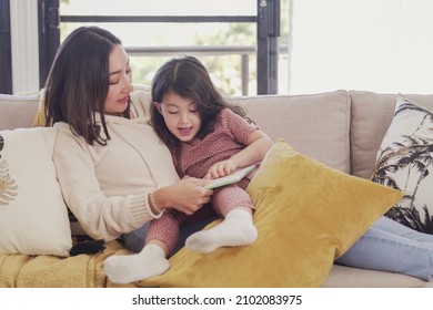 Asian mother read book to her mixed daughter girl at home, spending family quality time together, homeschooling education concept