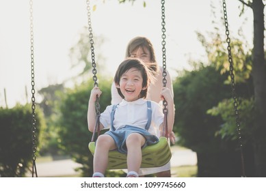 Asian Mother And Son Having Fun On Swing Together In The Park