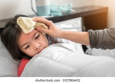 Asian mother take cool towel for reduce high fever on sick girl forehead on bed at morning time, Selective focus, Healthy and infection concept