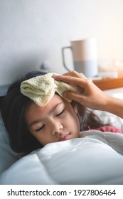 Asian Mother Take Cool Towel For Reduce High Fever On Sick Girl Forehead On Bed At Morning Time, Selective Focus, Healthy And Infection Concept