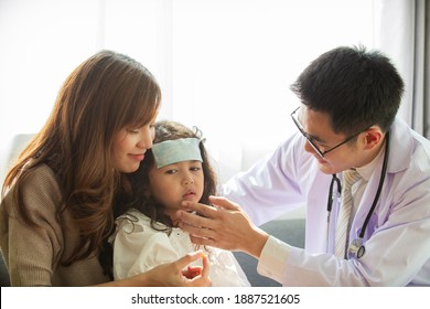 Asian Mother Takes Her Sick Young Daughter To See A Doctor In Hospital And Doctor Pasting A Cool Fever Gel On Girl's Forehead, Girl Got A Sickness From Flu Virus. Young Girl Patient Got A Sick.