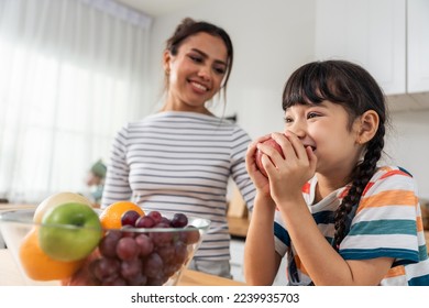 Asian mother teach and motivate young girl child eat healthy fruit. Adorable little kid child feel happy and relax, enjoy eat apple healthy foods for health care and wellness in kitchen at home. - Powered by Shutterstock