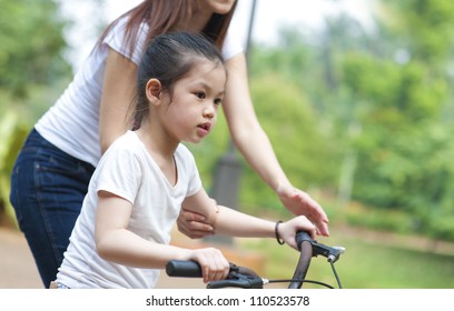 Asian Mother teaching daughter cycling at the park in the evening