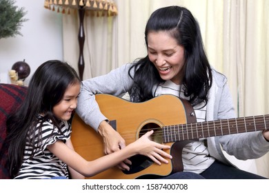 The Asian Mother Teaching Her Child To Play Guitar.