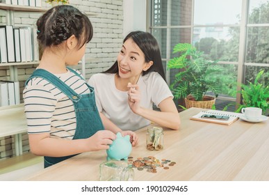Die asiatische Mutter unterrichtet ihre Tochter über finanzielle Ersparnisse und Geldmanagement mit Sparschwein und Spardose.