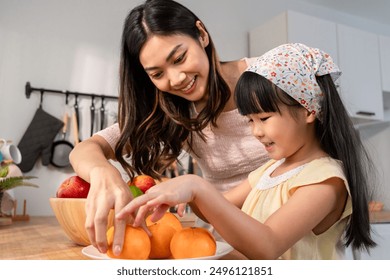 Asian mother teaching and motivate young girl child eat healthy fruit. Adorable little kid daughter feel happy and relax, enjoy eat apple healthy foods for health care and wellness in kitchen at home. - Powered by Shutterstock