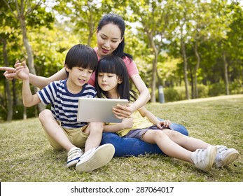 Asian Mother And Two Children Using Tablet Computer Outdoors.