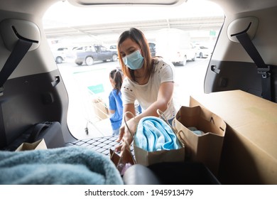Asian mother and two daughters wearing protection mask helping to put stuffs in the shopping trolley into trunk of car together in parking during coronavirus pandemic as new normal lifestyle. - Shutterstock ID 1945913479