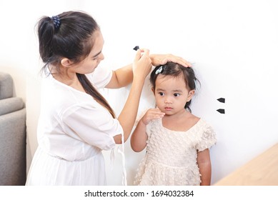 Asian Mother Use Tape For Measure Her Daughter's Height. Mom And Kids, Education, Family Relationship, Child Care, Children Growth Evolution Concept.
