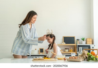 Asian mother wakes up in pajamas, puts her hair in a crown, makes her cute daughter have fun, cracks eggs, cooks baking, mixes flour, makes cakes and bakes in the kitchen at home. 