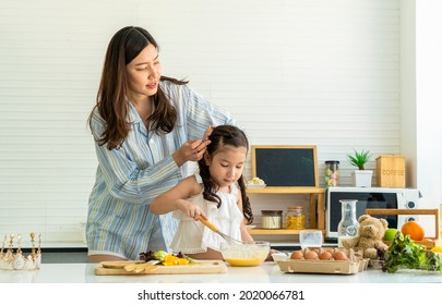 Asian mother wakes up wearing pajamas, makes her daughter's hair happy and has fun. Cracking eggs, baking, mixing ingredients, baking cakes and microwave in the kitchen at home. 