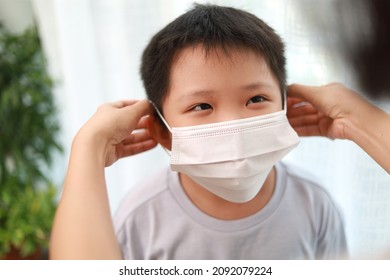 An Asian Mother Wearing A Protective Face Mask For Her Son Before Leaving House To School.