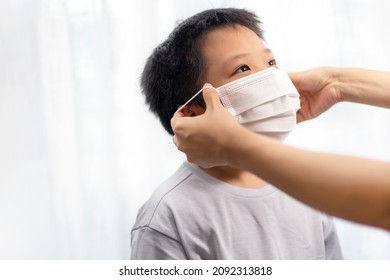 An Asian Mother Wearing A Protective Face Mask For Her Son Before Leaving House To School.