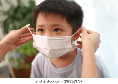 An Asian Mother Wearing A Protective Face Mask For Her Son Before Leaving House To School.