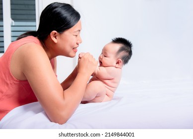 Asian Mothet Happy Playing With Her Daughter, Baby Newborn Is 3 Months Old On White Bed, With White Background, To Relationship Asain Family And Newborn Child Development Concept.