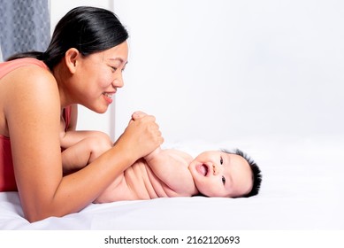 Asian Mothet Happy Playing With Her Daughter, Baby Newborn Is 3 Months Old On White Bed, With White Background, To Relationship Asain Family And Newborn Child Development Concept.