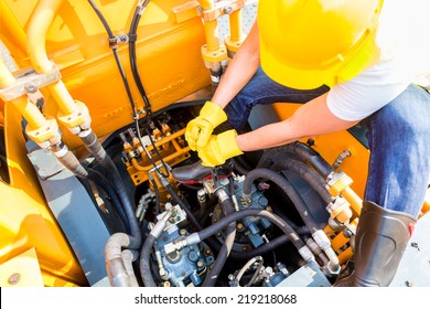 Asian motor mechanic working on construction or mining machinery in vehicle workshop