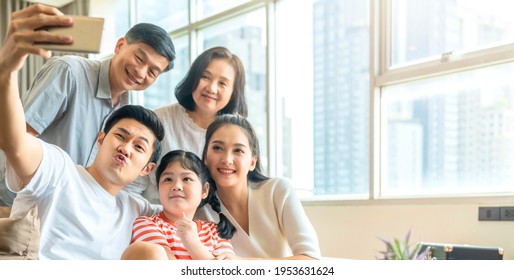 asian multi generation family parent and grand parent with little daughter child sit relax on sofa in living room take selfie with smartphone together with smiling and cheerful laugh smile at home