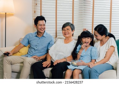 Asian Multi Generational Family Of Father, Mother, Daughter, And Grandmother Watching TV On Sofa In The Living Room