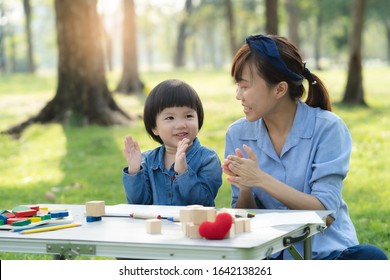 Asian Mum And Daughter Drawing On Paper In Garden.