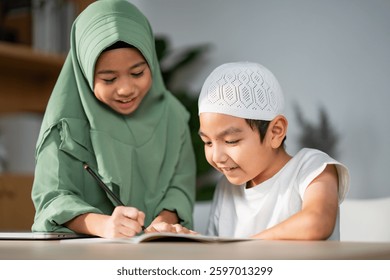 Asian Muslim boy and girl do homework together at home, Student electronic learning with happiness. Childs studying, teaching each other with smile.
