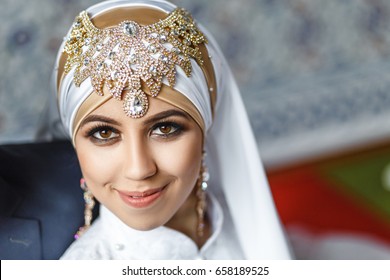 Asian Muslim bride in white decorated with golden arabic jewelry hijab and scarf, concept of oriental wedding