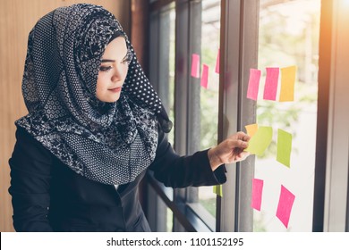 Asian Muslim Business Woman Hand Picking Sticky Notes On Glass Wall.