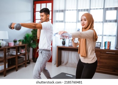 Asian Muslim Couple Exercising And Lifting Weight Dumbell At Home. Husband And Wife Workout Together