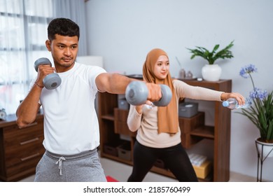 Asian Muslim Couple Exercising And Lifting Weight Dumbell At Home. Husband And Wife Workout Together