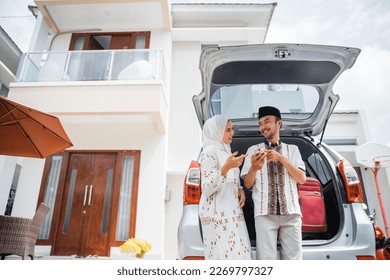 Asian Muslim couple using cell phone together and preparing in car in front of house for homecoming trip - Powered by Shutterstock