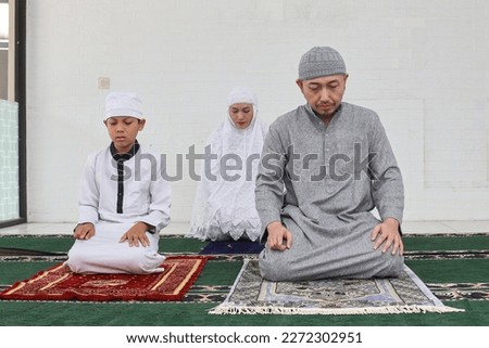 Asian muslim family praying salah jamaah together at home, last movement on salat procedure. The worshiper proceeds to sit and recite the tashahhud, salawat and other prayers. 