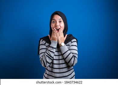 Asian Muslim Girl Wearing Hijab Shows Surprised Or Shocked Expression With Open Mouth, Close Up Facial Expression Over Blue Background