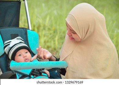 Asian Muslim Hijabi Mother And Father Walk Through The Park With Son In Stroller While His Mom Taking Care Of Her Todler