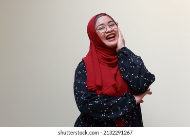 An Asian Muslim Lady Standing With One Hand On Her Cheek And Laughing.