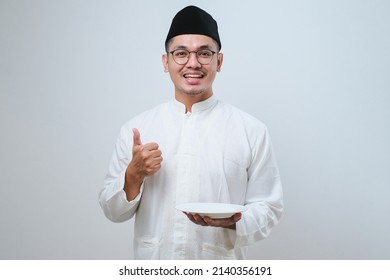 Asian muslim man giving thumb up while holding empty dinner plate over white background