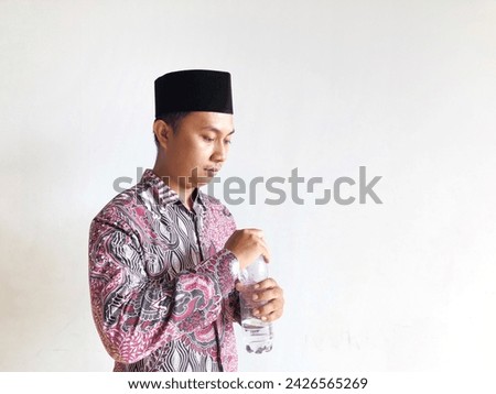 Asian muslim man holding plastic water bottle on isolated background